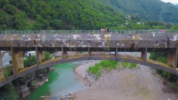 4人で構成される会社は ジョージア州の山や川を背景に峡谷を渡る大きなコンクリートの歩道橋を渡っています 観光客は地域を探索し 古代の橋のドローンの形でランドマーク — ストック動画