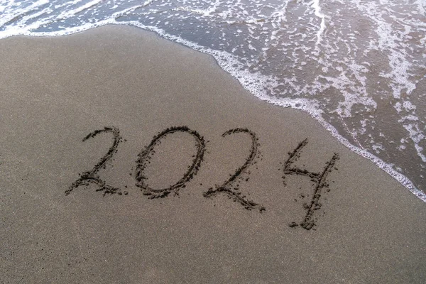 Text Happy New Year 2024 on a sandy sea beach with a small wave. Abstract background photo of the upcoming New Year 2023