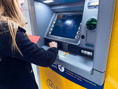 KALAMATA, GREECE - 2022 JANUARY: Genç bayan Kalamata şehrindeki kapalı bir Pire Bankası 'nın önünde nakit para makinesi kullanın. ATM 'den para çeken kadın.