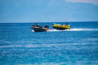 Tourists enjoy inflatable towable rides at Koukounaries beach in Skiathos island, Sporades, Greece
