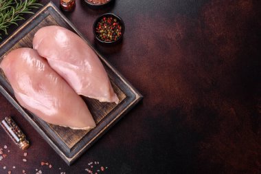 Kesme tahtasında çiğ tavuk filetosu ve arka planda baharatlar. Üst görünüm