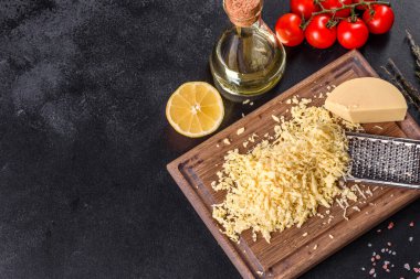 Koyu beton arka planda tahta kesme tahtasındaki büyük rende rendelenmiş taze sert peynir.