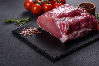 Kesme tahtasındaki çiğ domuz bifteği, otlar ve baharatlar koyu taş masada.