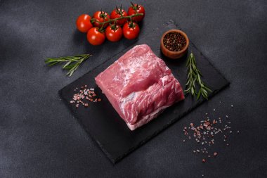 Kesme tahtasındaki çiğ domuz bifteği, otlar ve baharatlar koyu taş masada.