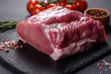 Kesme tahtasındaki çiğ domuz bifteği, otlar ve baharatlar koyu taş masada.