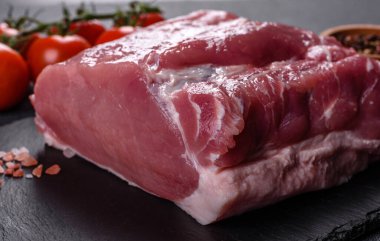 Kesme tahtasındaki çiğ domuz bifteği, otlar ve baharatlar koyu taş masada.