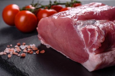 Kesme tahtasındaki çiğ domuz bifteği, otlar ve baharatlar koyu taş masada.