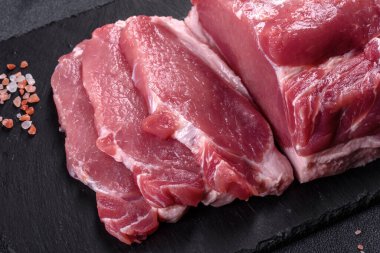 Kesme tahtasındaki çiğ domuz bifteği, otlar ve baharatlar koyu taş masada.