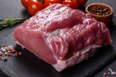 Kesme tahtasındaki çiğ domuz bifteği, otlar ve baharatlar koyu taş masada.