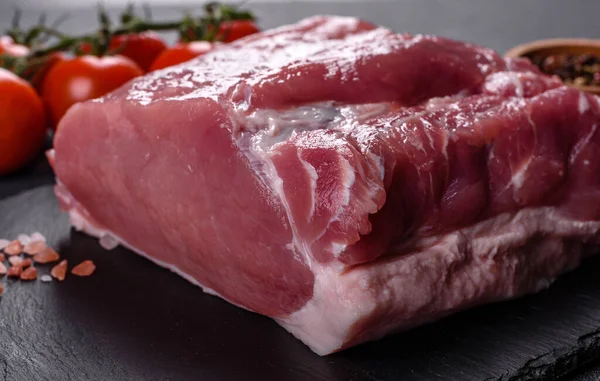 Kesme tahtasındaki çiğ domuz bifteği, otlar ve baharatlar koyu taş masada.