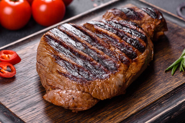 Cooked grilled Chuck eye roll steak on a chopping Board. Dark background