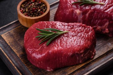 Kesme tahtasında çiğ biftek ve arka planda baharatlar.