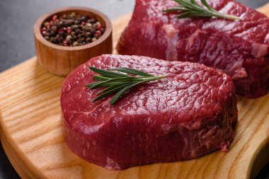 Kesme tahtasında çiğ biftek ve arka planda baharatlar.
