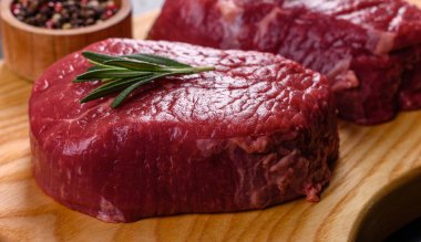 Kesme tahtasında çiğ biftek ve arka planda baharatlar.