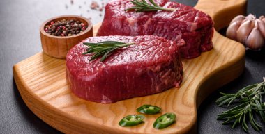 Kesme tahtasında çiğ biftek ve arka planda baharatlar.