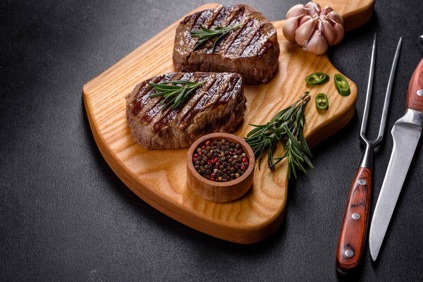 Fresh juicy delicious beef steak on a dark background. Meat dish with spices and herbs