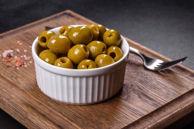 Beautiful pickled green olives on a dark concrete background. Preparation of the festive table