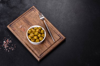 Beautiful pickled green olives on a dark concrete background. Preparation of the festive table