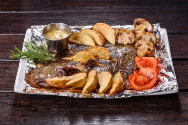 Beyaz dikdörtgen bir tabakta patates ve domatesli lezzetli kızarmış balık. Festival masasının hazırlığı