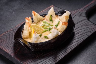 Peynir ve ekmek kırıntılarıyla pişirilmiş lezzetli bir deniz ürünleri tabağı. Baharat ve otlarla dolu dökme demir bir kasede.