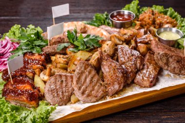 Ahşap tepside baharat ve otlarla pişirilmiş birkaç çeşit et. Büyük bir şirket için masa hazırlanıyor.