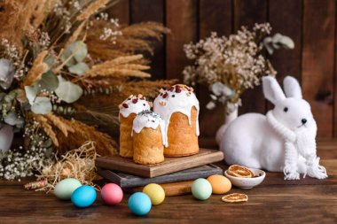 Paskalya pastası ve yumurtalar farklı renklerde boyanmış ve tahta arka planda Paskalya tavşanı var.