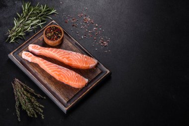 Somon balığı. Pişirme malzemeleri ve siyah arka planda bitkilerle taze çiğ somon balığı filetosu.