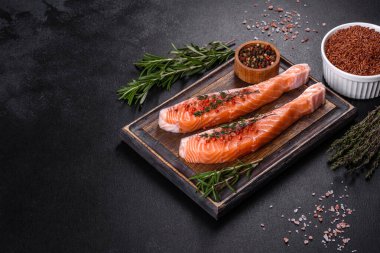 Somon balığı. Pişirme malzemeleri ve siyah arka planda bitkilerle taze çiğ somon balığı filetosu.