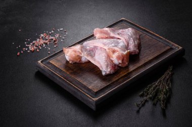 Çiğ et. Tavuk kanatları ahşap bir tahtada, sebzeler ve baharatlar siyah arka planda.