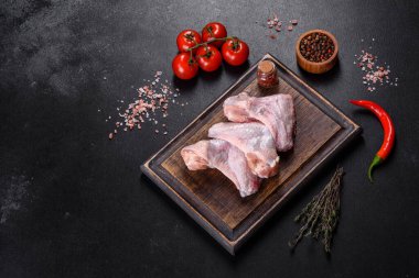 Çiğ et. Tavuk kanatları ahşap bir tahtada, sebzeler ve baharatlar siyah arka planda.