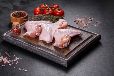 Çiğ et. Tavuk kanatları ahşap bir tahtada, sebzeler ve baharatlar siyah arka planda.