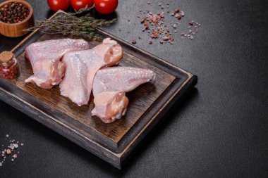 Çiğ et. Tavuk kanatları ahşap bir tahtada, sebzeler ve baharatlar siyah arka planda.