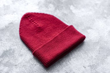 Beton bir arka planda kırmızı, sıcak örülmüş kadın şapkası. Hobiler ve boş zaman