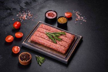 Ahşap bir tahtanın üzerinde pişmemiş çiğ et ve kuzu eti kebabı sosisi. Siyah arkaplan