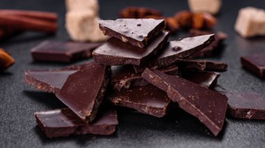 Siyah zemin üzerinde yıldız anason ve tarçın olan kırık siyah çikolata parçaları.
