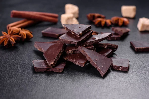 Siyah zemin üzerinde yıldız anason ve tarçın olan kırık siyah çikolata parçaları.