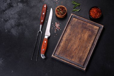 Kahverengi dikdörtgen ahşap kesme tahtası. Koyu beton arka planda tuz ve baharatlar var. Evde yemek pişirmek.