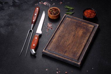 Kahverengi dikdörtgen ahşap kesme tahtası. Koyu beton arka planda tuz ve baharatlar var. Evde yemek pişirmek.