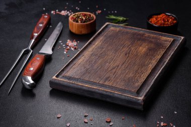 Kahverengi dikdörtgen ahşap kesme tahtası. Koyu beton arka planda tuz ve baharatlar var. Evde yemek pişirmek.