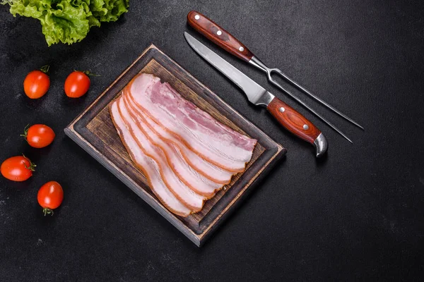 Tahta kesme tahtasındaki pastırma dilimleri. Domuz eti. Siyah arka plan. Üst görünüm