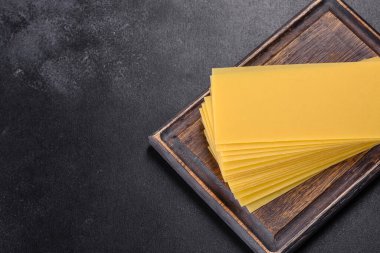 Koyu beton arka planda bitkiler ve baharatlarla dolu bir yığın çiğ lazanya.