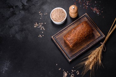 Taze pişmiş kahverengi ekmek, kulakları ve çimento üzerinde buğday taneleri.