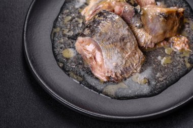 Siyah yuvarlak bir tabakta koyu beton bir arka planda yağda konserve sardalya. Lezzetli bir atıştırmalık