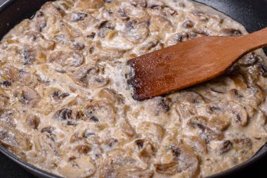 Lezzetli taze şampiyonlar, siyah bir tavada kaynatılmış kremalı sosla dilimlenmiş.