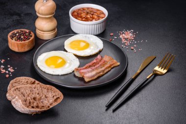 Yağda yumurta, pastırma, fasulye, domates, baharat ve bitkilerle İngiliz kahvaltısı. Güne doyurucu ve doyurucu bir başlangıç.