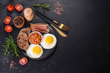 Yağda yumurta, pastırma, fasulye, domates, baharat ve bitkilerle İngiliz kahvaltısı. Güne doyurucu ve doyurucu bir başlangıç.