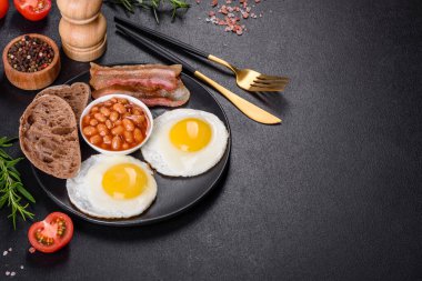 Yağda yumurta, pastırma, fasulye, domates, baharat ve bitkilerle İngiliz kahvaltısı. Güne doyurucu ve doyurucu bir başlangıç.