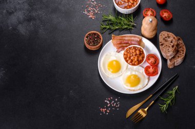 Yağda yumurta, pastırma, fasulye, domates, baharat ve bitkilerle İngiliz kahvaltısı. Güne doyurucu ve doyurucu bir başlangıç.