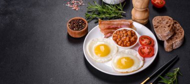 Yağda yumurta, pastırma, fasulye, domates, baharat ve bitkilerle İngiliz kahvaltısı. Güne doyurucu ve doyurucu bir başlangıç.