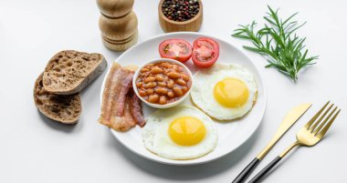 Yağda yumurta, pastırma, fasulye, domates, baharat ve bitkilerle İngiliz kahvaltısı. Güne doyurucu ve doyurucu bir başlangıç.